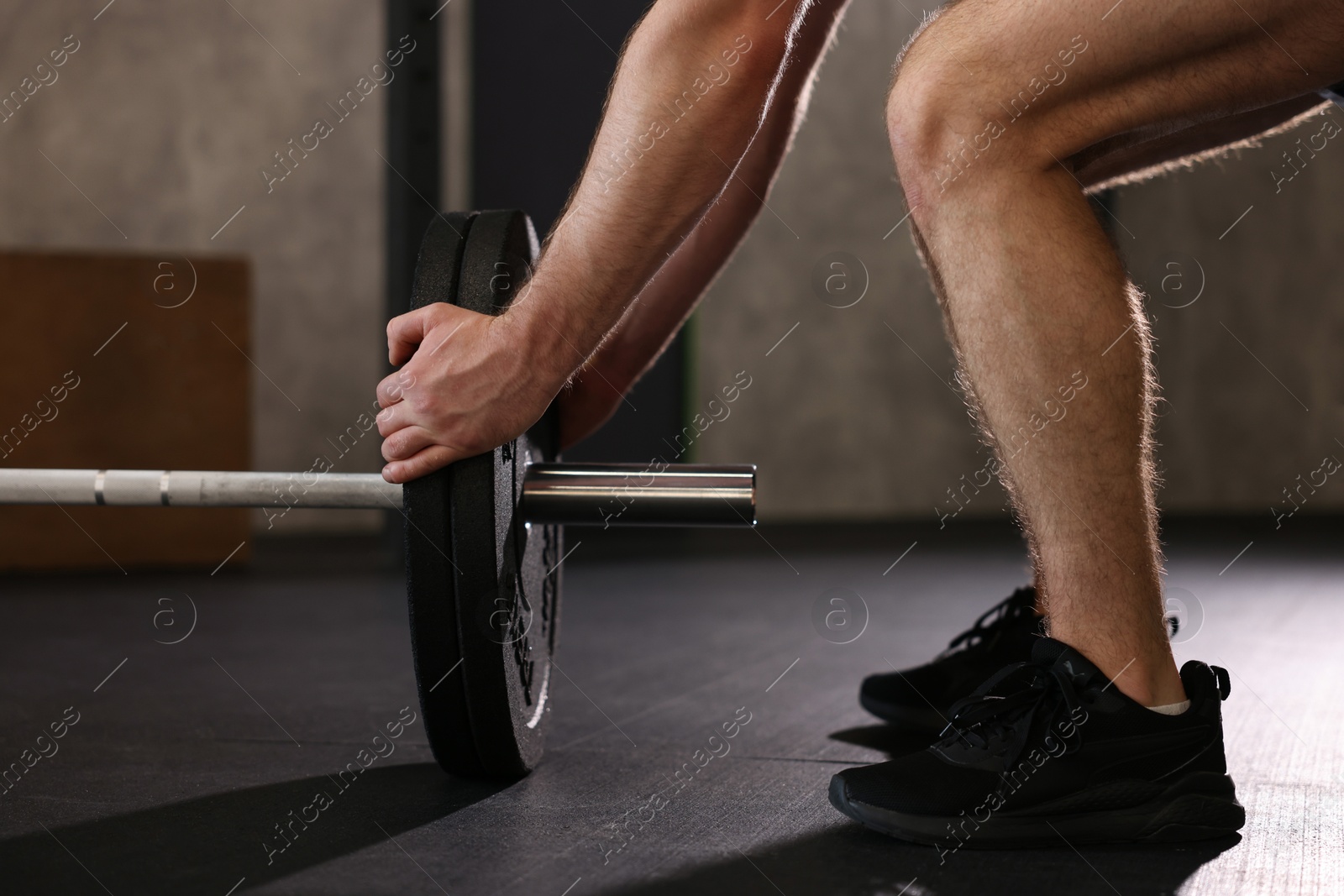 Photo of Sportsman putting weights on barbell before crossfit workout in gym, closeup