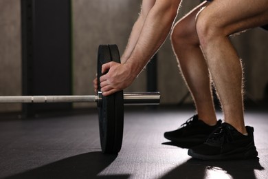 Photo of Sportsman putting weights on barbell before crossfit workout in gym, closeup