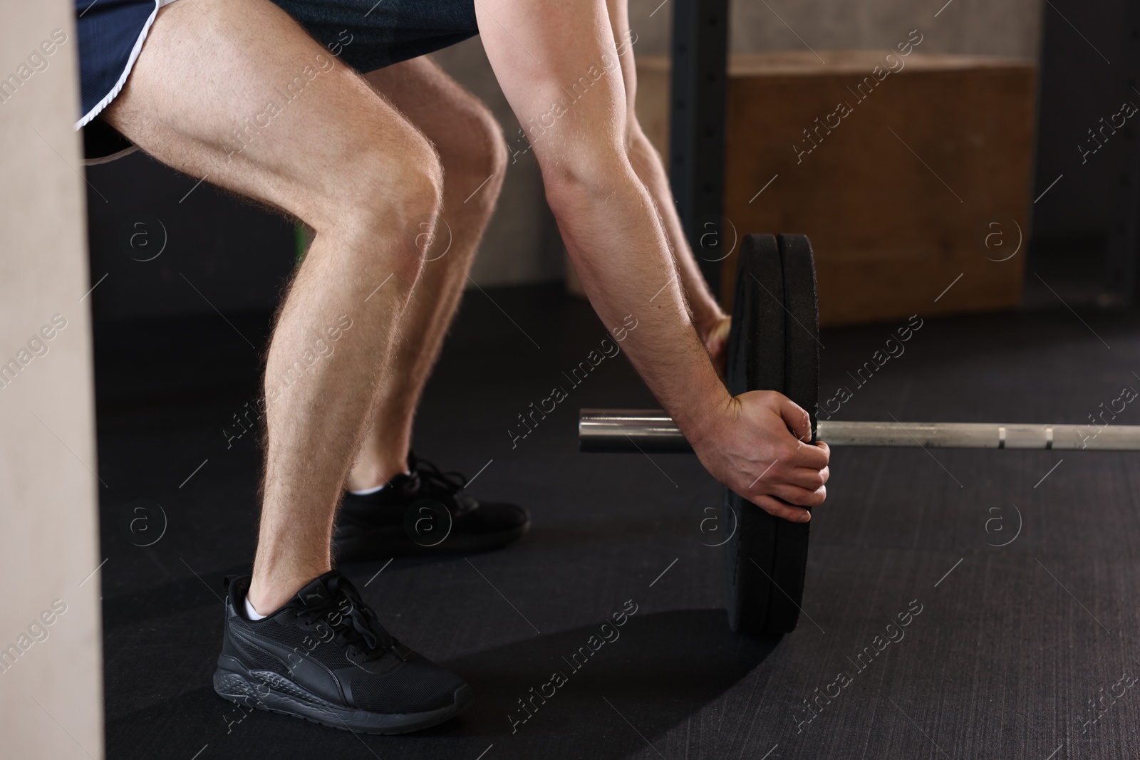 Photo of Sportsman putting weights on barbell before crossfit workout in gym, closeup