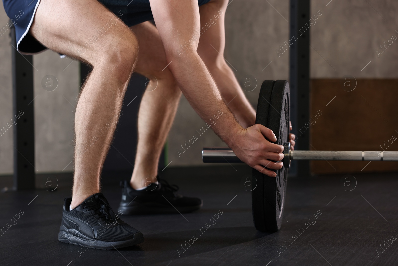 Photo of Sportsman putting weights on barbell before crossfit workout in gym, closeup