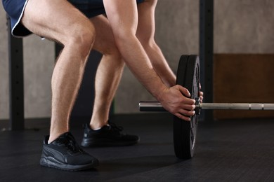 Photo of Sportsman putting weights on barbell before crossfit workout in gym, closeup