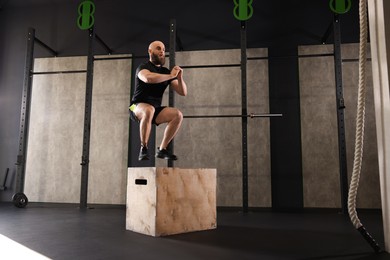 Photo of Sportsman doing box jumping during crossfit workout in gym