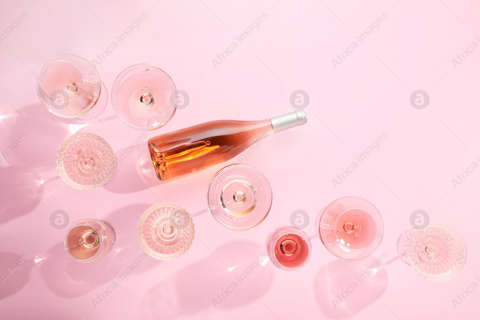 Photo of Delicious rose wine in glasses and bottle on pink background, flat lay. Space for text