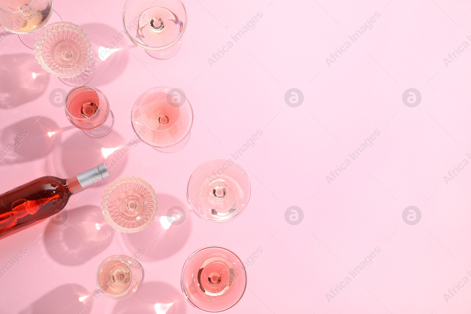 Photo of Delicious rose wine in glasses and bottle on pink background, flat lay. Space for text