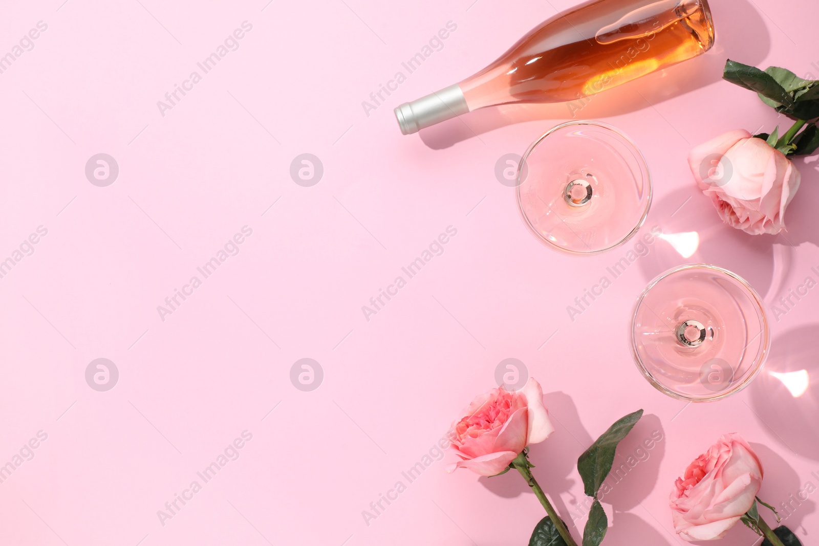 Photo of Delicious rose wine in glasses and bottle with flowers on pink background, flat lay. Space for text