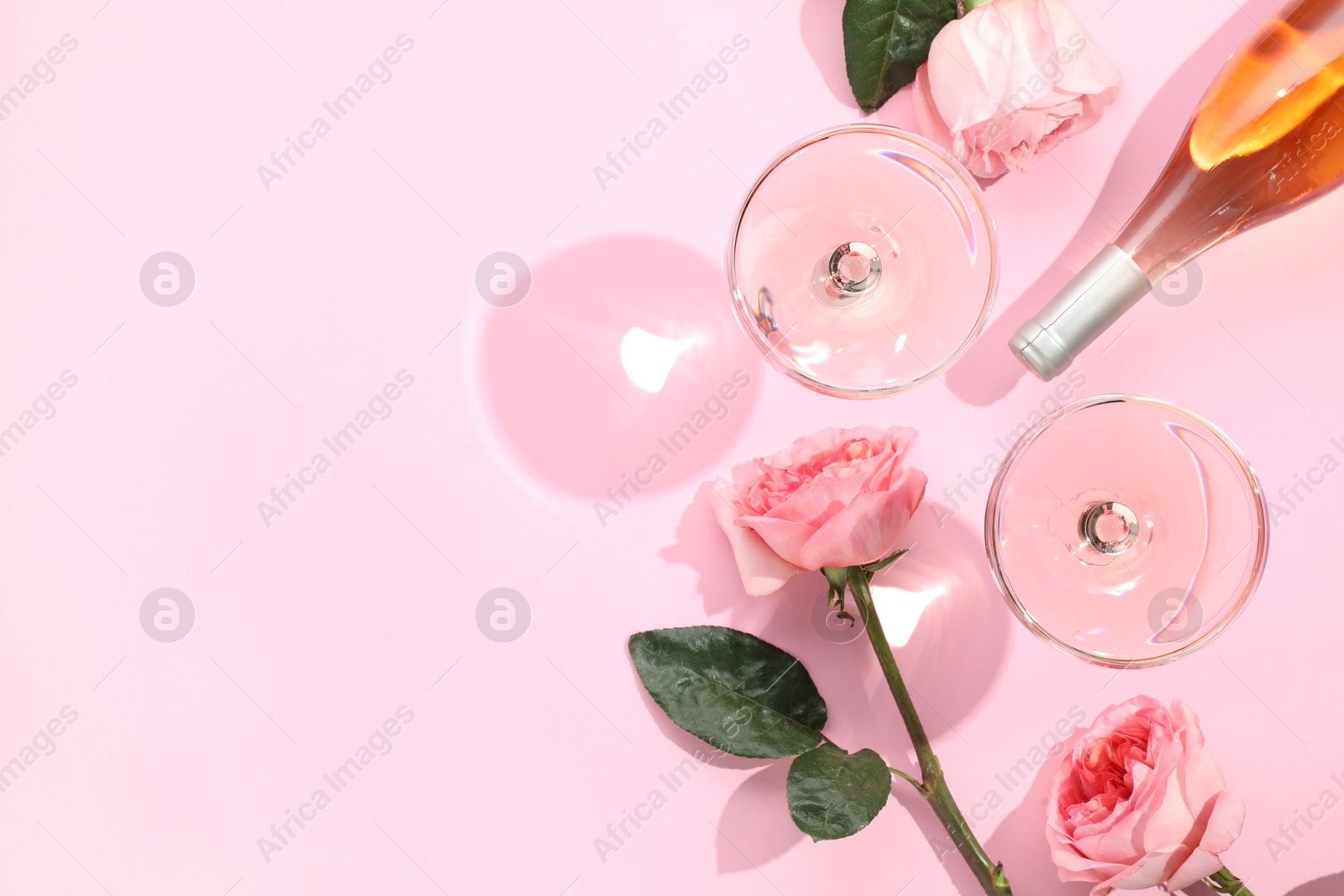 Photo of Delicious rose wine in glasses and bottle with flowers on pink background, flat lay. Space for text