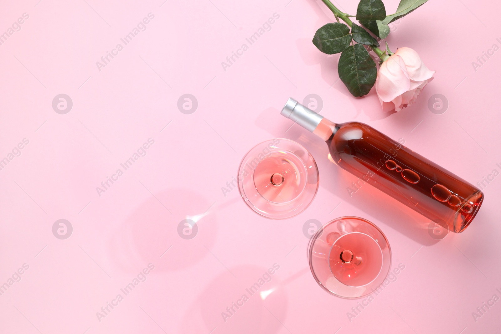 Photo of Delicious rose wine in glasses and bottle with flower on pink background, flat lay. Space for text