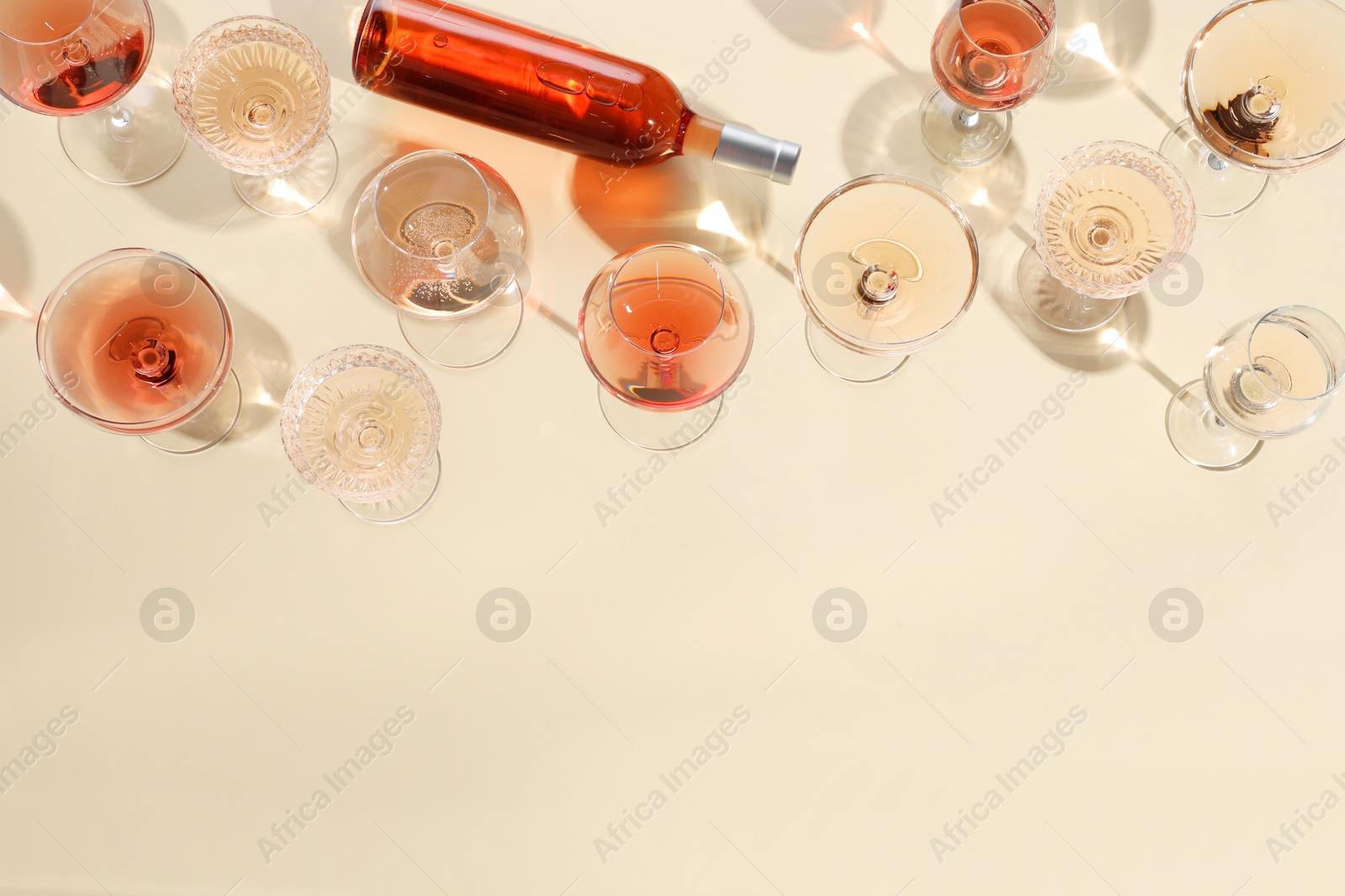 Photo of Delicious rose wine in glasses and bottle on beige background, flat lay. Space for text