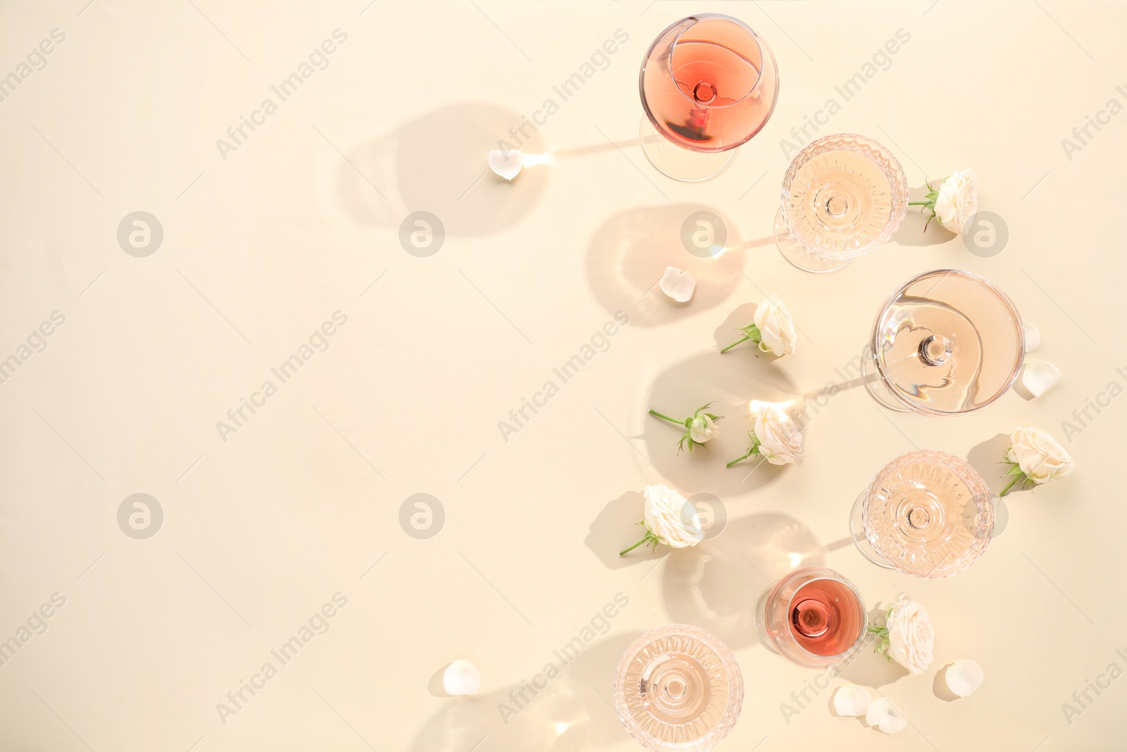 Photo of Delicious rose wine in glasses and flowers on beige background, flat lay. Space for text