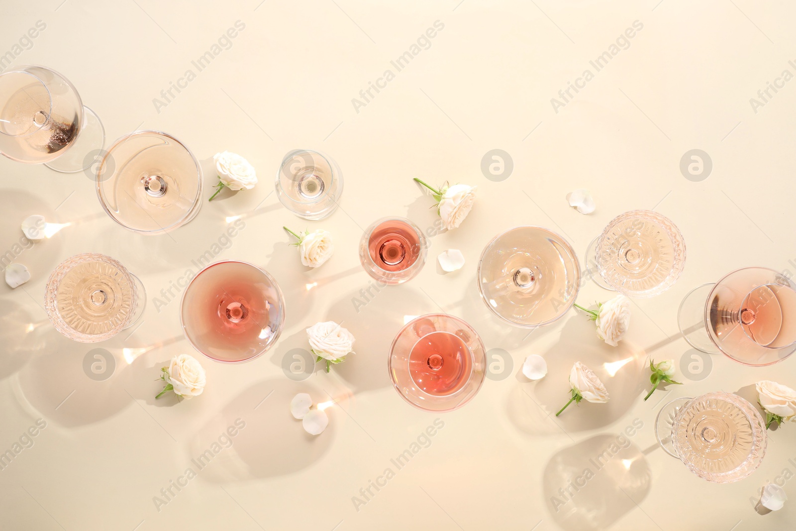 Photo of Delicious rose wine in glasses and flowers on beige background, flat lay. Space for text