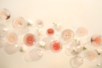 Delicious rose wine in glasses and flowers on beige background, flat lay. Space for text