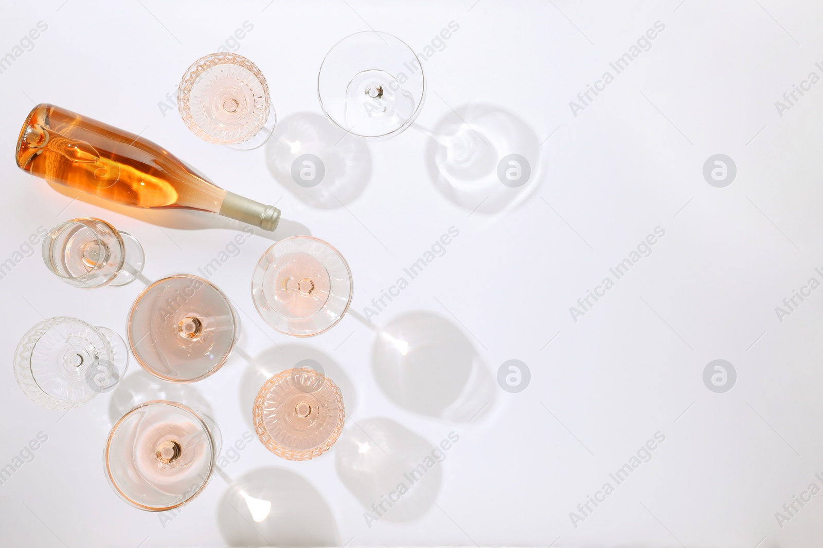 Photo of Delicious rose wine in glasses and bottle on white background, flat lay. Space for text