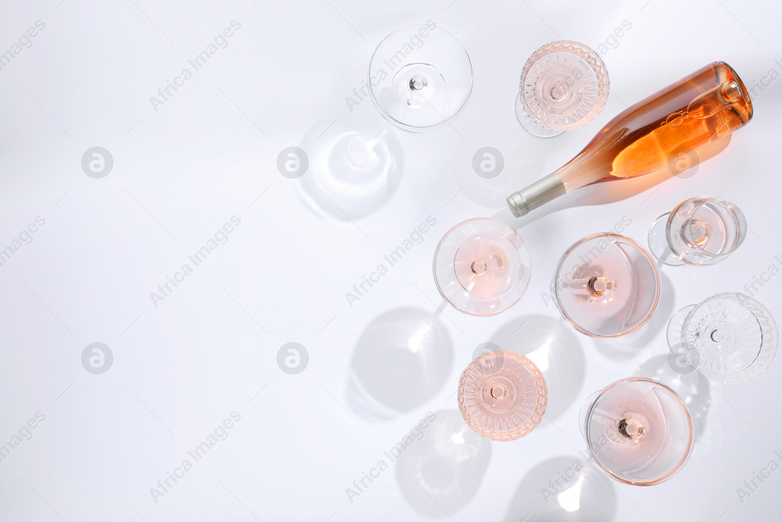 Photo of Delicious rose wine in glasses and bottle on white background, flat lay. Space for text