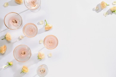 Delicious rose wine in glasses and flowers on white background, flat lay. Space for text