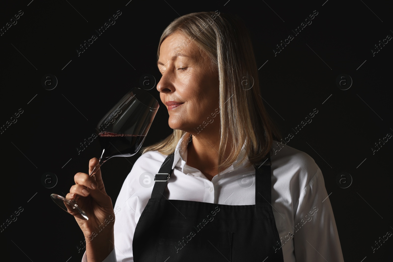 Photo of Professional sommelier tasting red wine on black background