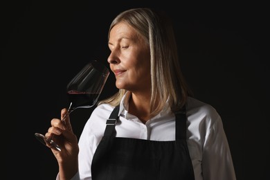 Photo of Professional sommelier tasting red wine on black background