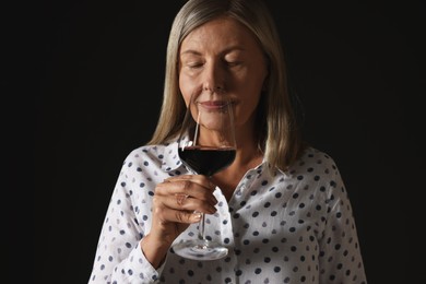 Photo of Professional sommelier tasting red wine in glass on black background