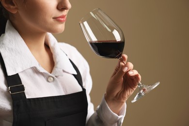 Photo of Professional sommelier tasting red wine in glass on beige background, closeup