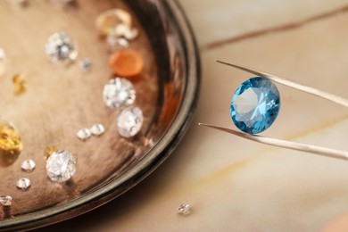 Photo of Tweezers with beautiful gemstones on light table, selective focus