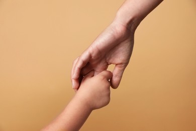 Photo of Mother and child holding hands on beige background, closeup