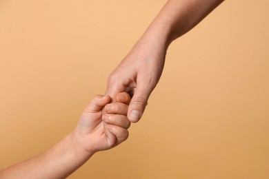 Photo of Mother and child holding hands on beige background, closeup