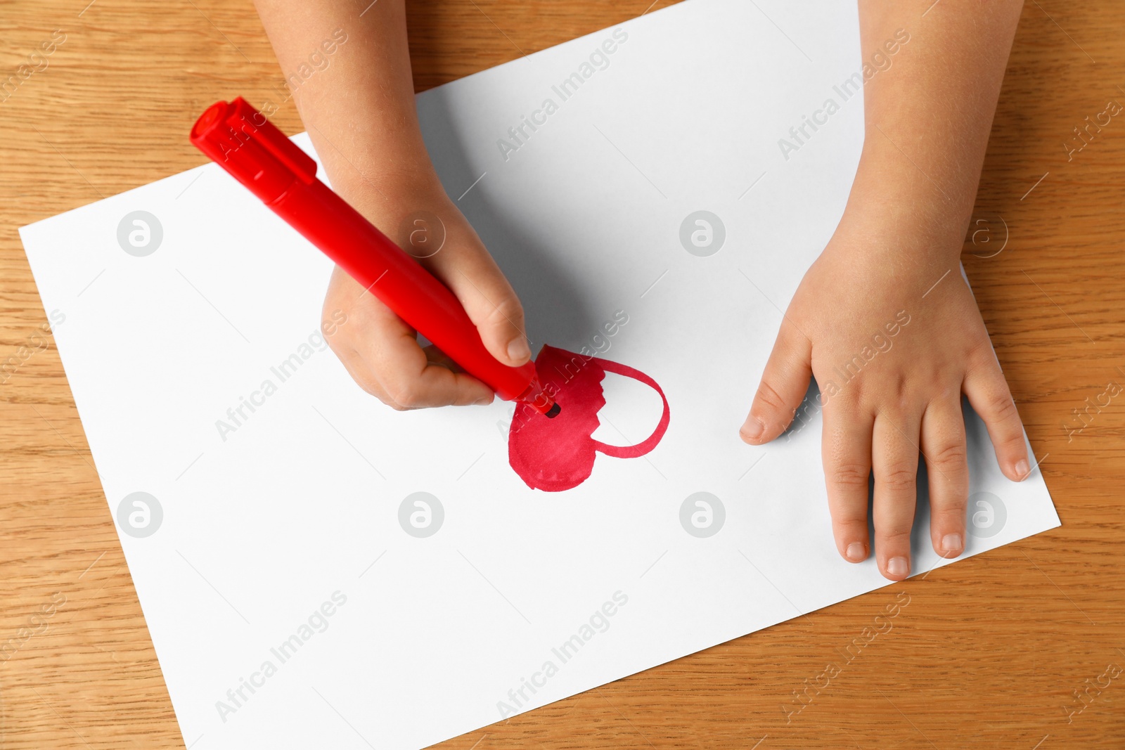 Photo of Little child drawing heart with felt tip pen at wooden table, top view