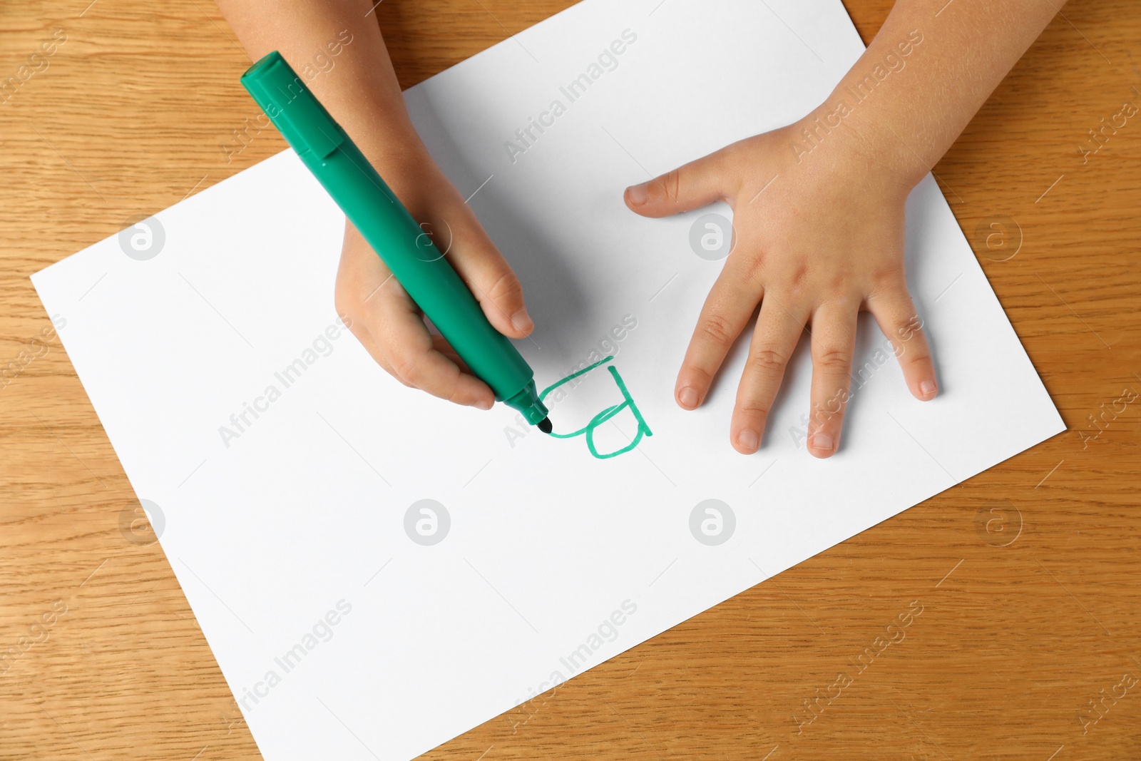 Photo of Little child writing letter B on paper sheet at wooden table, top view