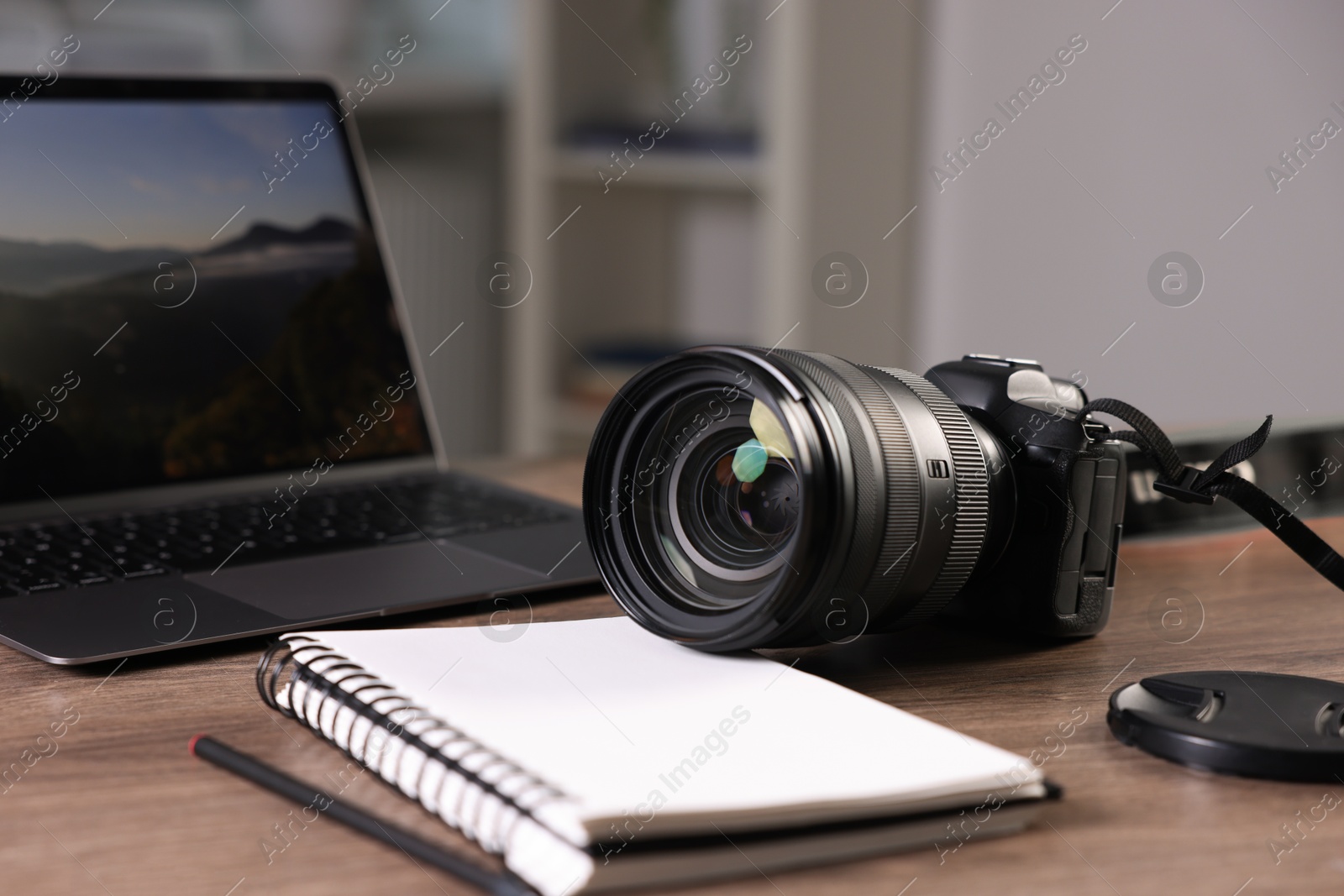 Photo of Professional photo camera, laptop and notepad on wooden desk indoors, closeup