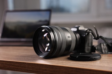 Photo of Professional photo camera and laptop on wooden desk indoors, selective focus