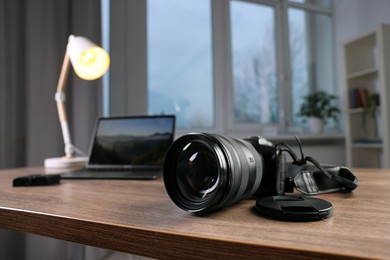 Photo of Professional photo camera and laptop on wooden desk indoors, selective focus. Space for text