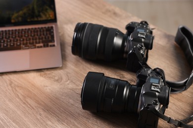 Photo of Professional photo cameras and laptop on wooden desk, closeup