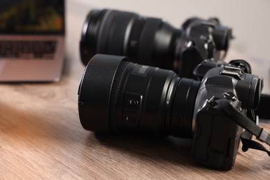 Photo of Professional photo cameras and laptop on wooden desk, closeup