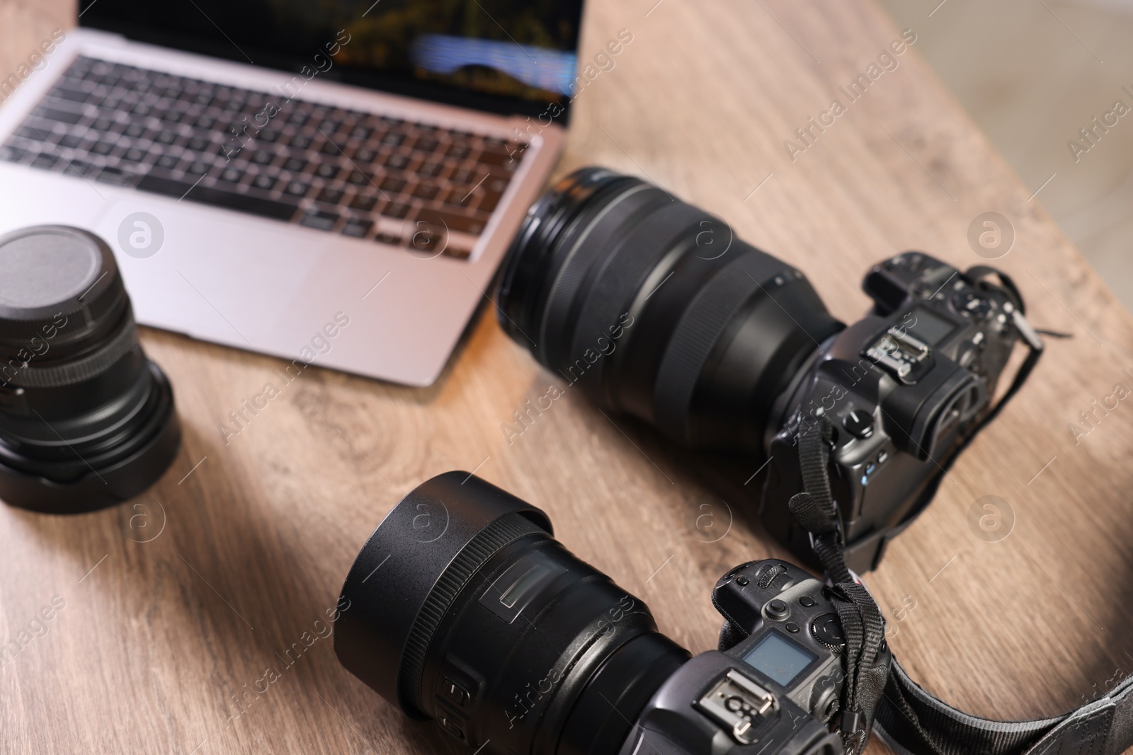 Photo of Professional photo cameras and laptop on wooden desk, closeup