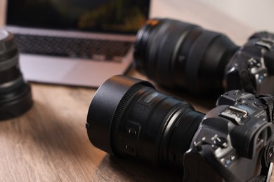 Photo of Professional photo cameras and laptop on wooden desk, closeup