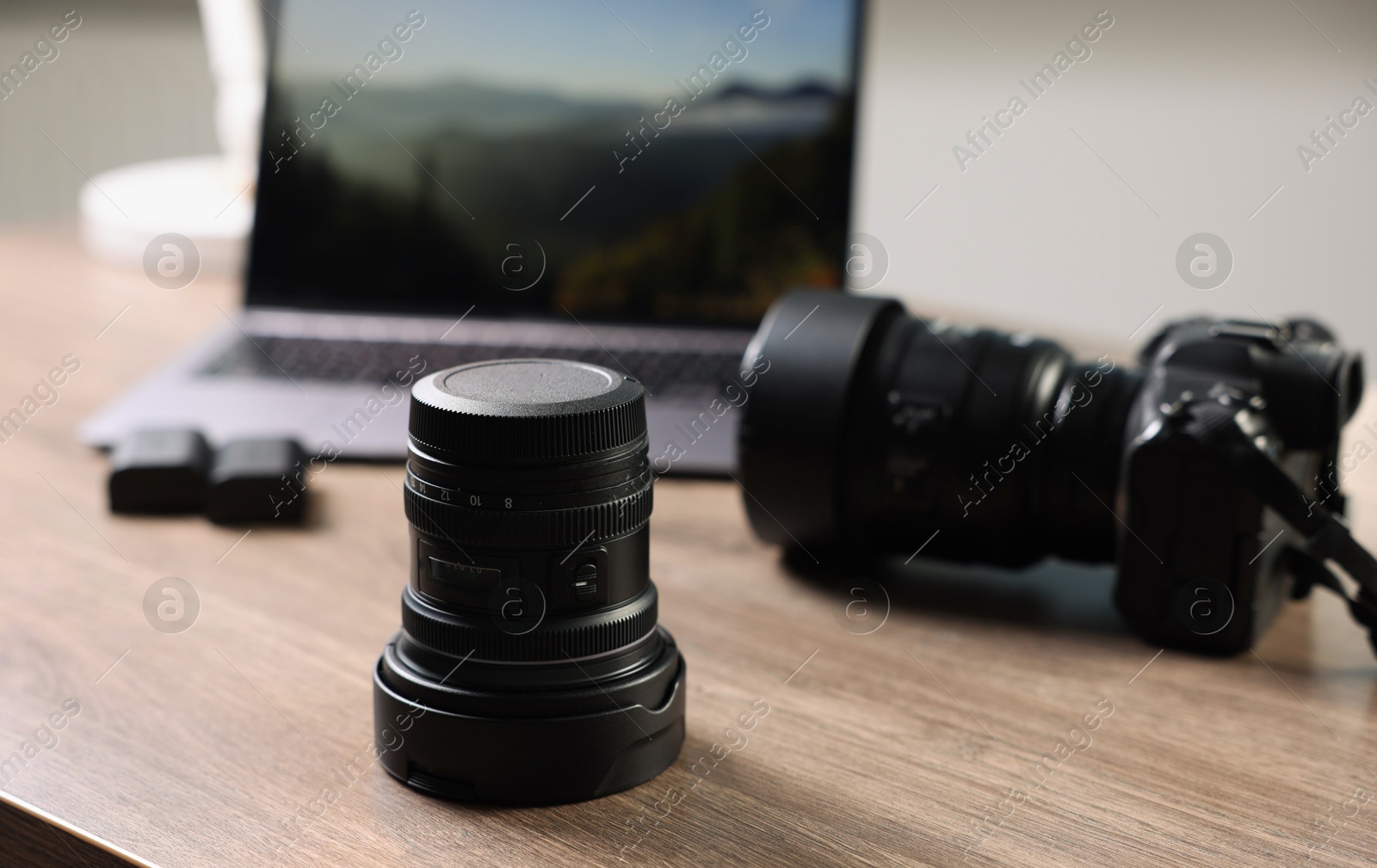 Photo of Professional photo camera, lens and laptop on wooden desk, selective focus