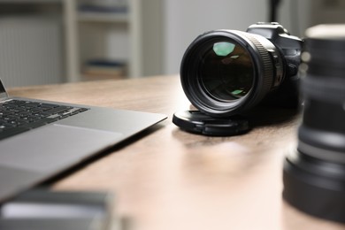 Photo of Professional photo camera, lens and laptop on wooden desk, selective focus