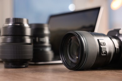 Photo of Professional photo camera, lenses and laptop on wooden desk indoors, selective focus