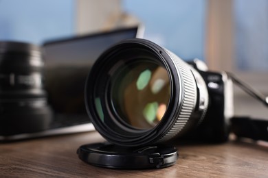 Photo of Professional photo camera and laptop on wooden desk indoors, selective focus