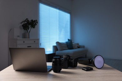 Photo of Professional photo camera, lens, flash and laptop on wooden desk indoors. Space for text