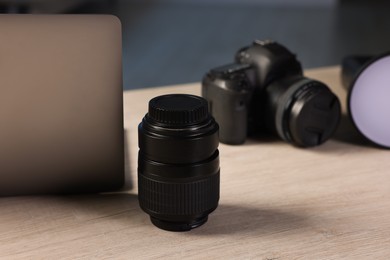 Photo of Professional photo camera, lens, flash and laptop on wooden desk indoors, selective focus