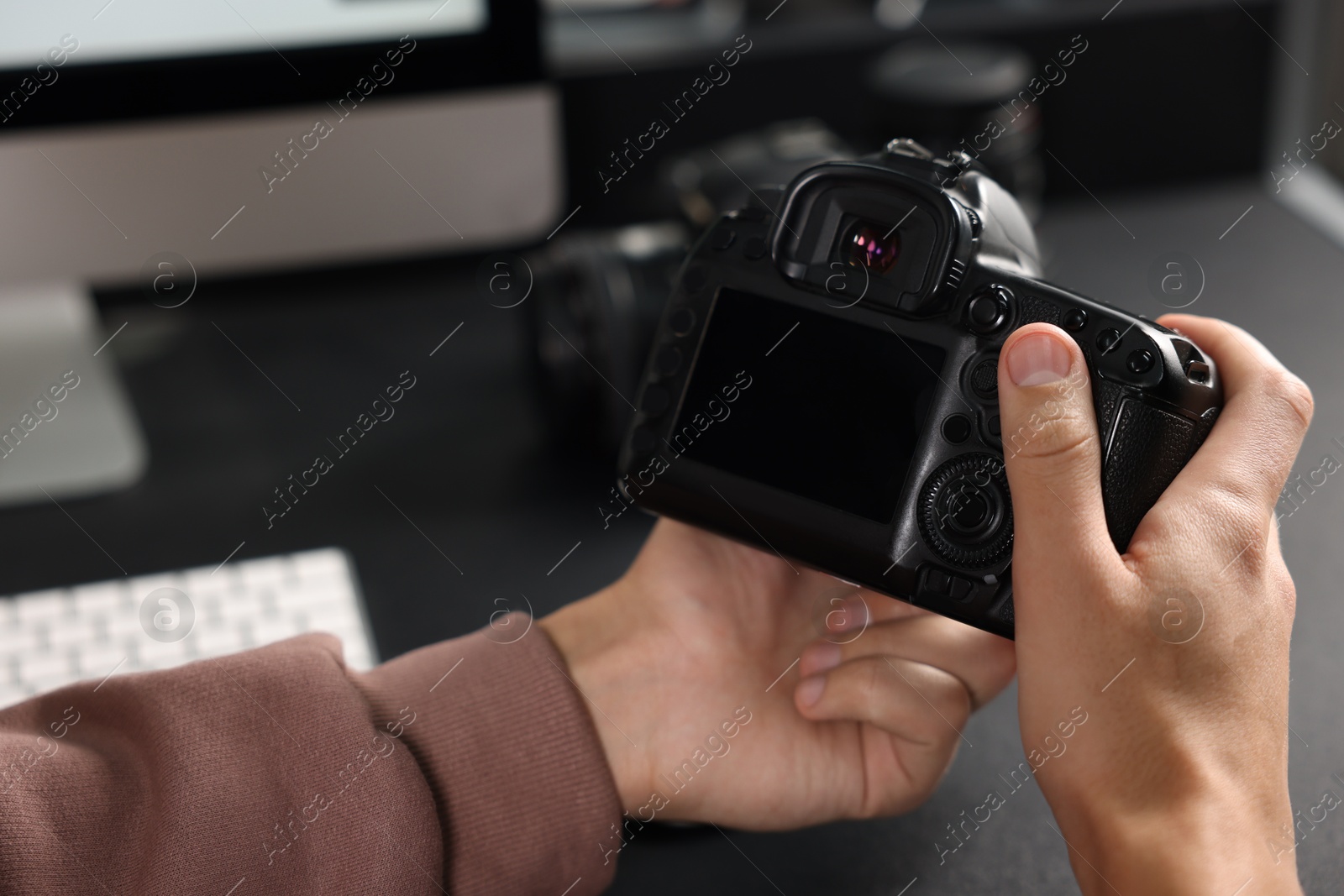 Photo of Photographer with professional camera at black desk indoors, closeup