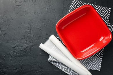 Photo of Red ceramic casserole and baking parchment paper on black table, top view. Space for text