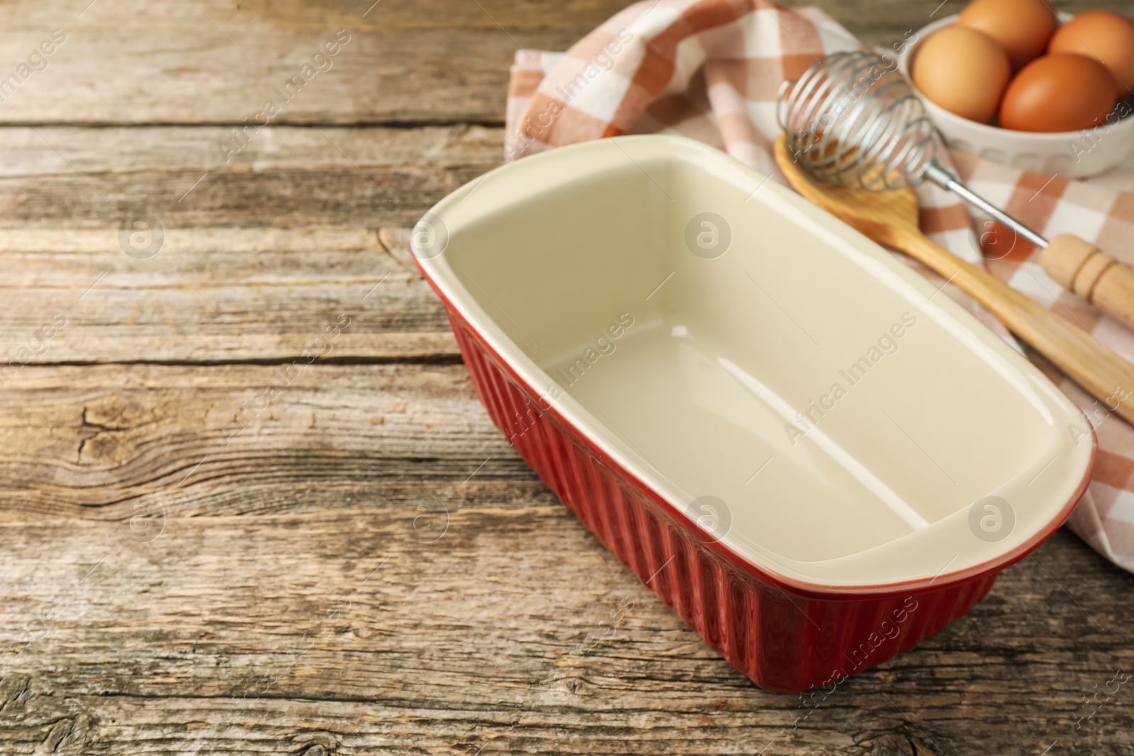 Photo of Ceramic casserole, whisk, spoon and eggs on wooden table, closeup. Space for text