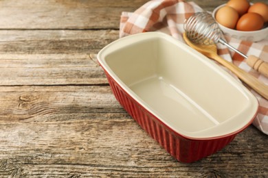 Photo of Ceramic casserole, whisk, spoon and eggs on wooden table, closeup. Space for text