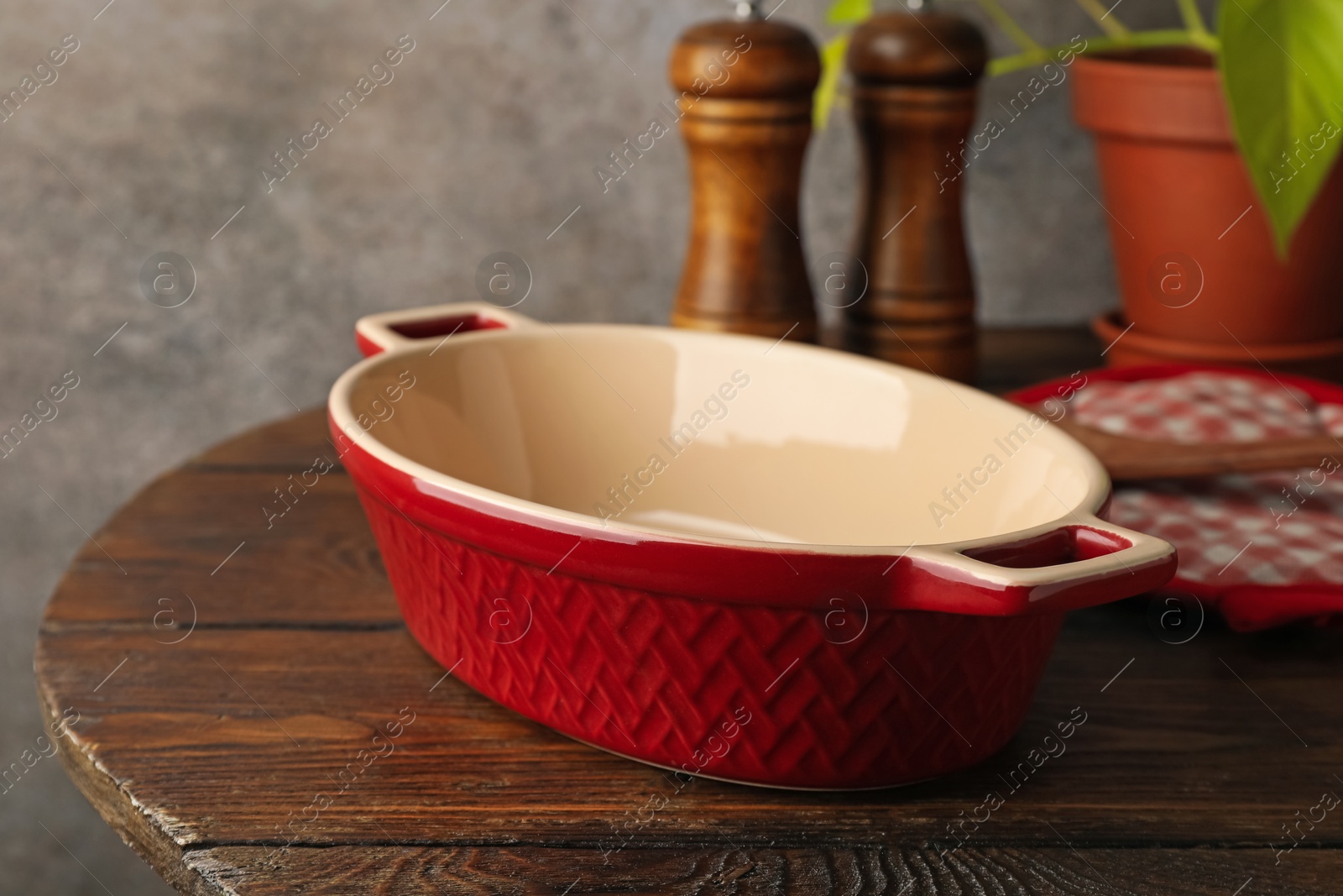 Photo of Ceramic casserole, potholder and shakers on wooden table, closeup