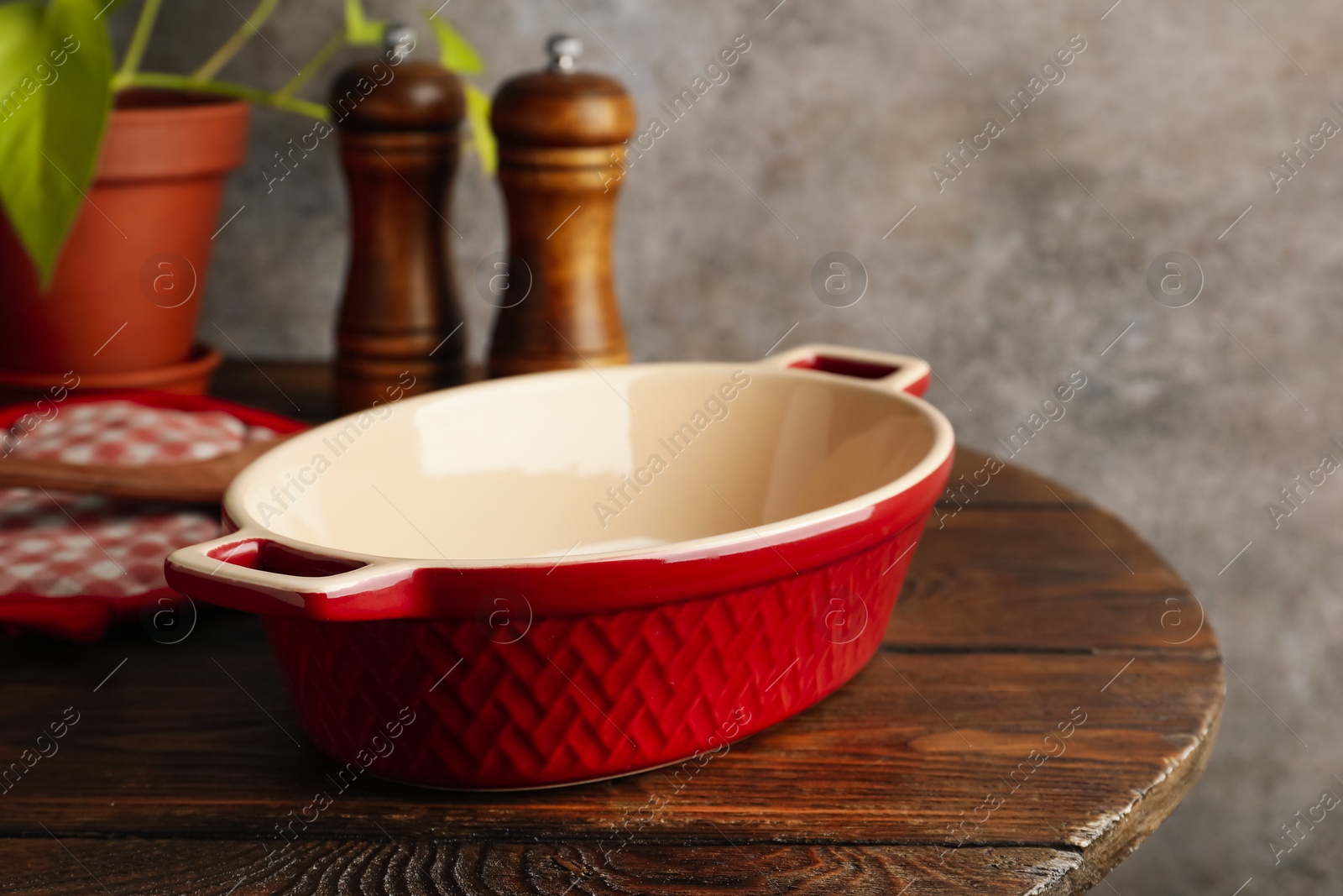 Photo of Ceramic casserole, potholder and shakers on wooden table, closeup