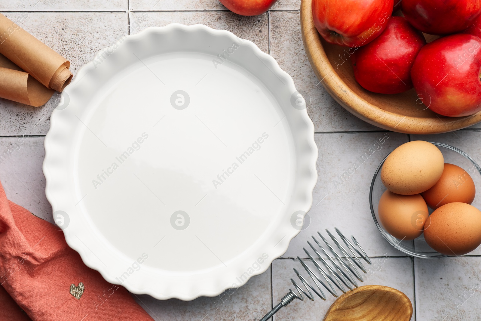 Photo of Ceramic casserole, different cooking utensils, apples and eggs on tiled table, flat lay