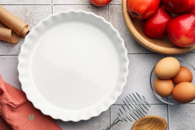 Photo of Ceramic casserole, different cooking utensils, apples and eggs on tiled table, flat lay