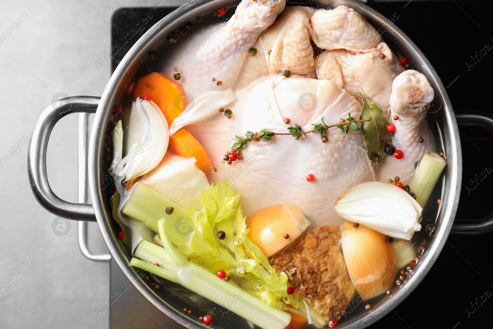 Photo of Whole fresh turkey, cut onion, carrot, celery, spices in pot and stove on grey table, top view