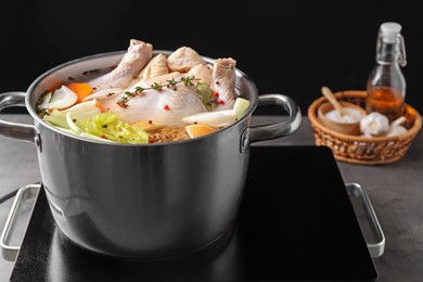 Photo of Whole fresh turkey, cut onion, celery, spices in pot and stove on grey table against black background, closeup